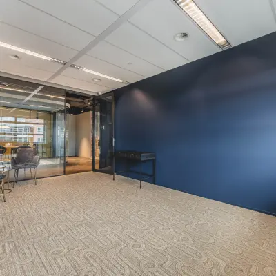 Moderne kantoorpandinterieur met glazen muur op Rijnzathe 12, De Meern. Geschikt voor het huren van flexibele kantoorruimte. De ruimte heeft een blauwe wand, stoelen en een tafel.
