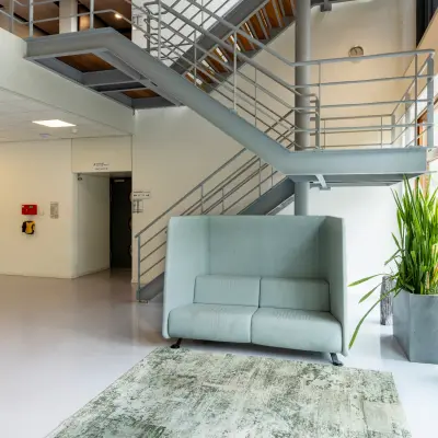 Ruime, lichte entree van een kantoorpand op Delftechpark 9, Delft. Grote ramen, grijze trap en moderne zitbank. Ideaal voor bedrijven die kantoorruimte willen huren met een professionele uitstraling.