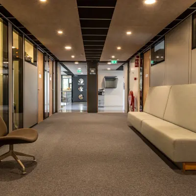 Kantoorruimte huren op Delftechpark 9 in Delft, met moderne grijze stoelen en banken in een ruime gang. Verlichte plafonds geven een heldere uitstraling aan de kantoorgang.