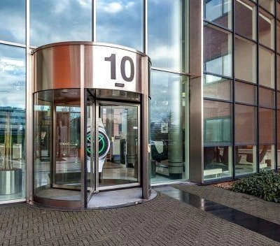 Hoofdingang van het kantoorpand op Olof Palmerstraat 10 in Delft met grote glazen gevel en draaideur, perfect voor diegene die kantoorruimte wil huren in een moderne omgeving.