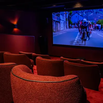 Een stijlvolle, donkere bioscoopzaal met comfortabele rode stoelen en een groot scherm met een wielerwedstrijd, ideaal voor ontspanning of presentaties in het kantoorpand op Reitschweg 1 in Den Bosch.