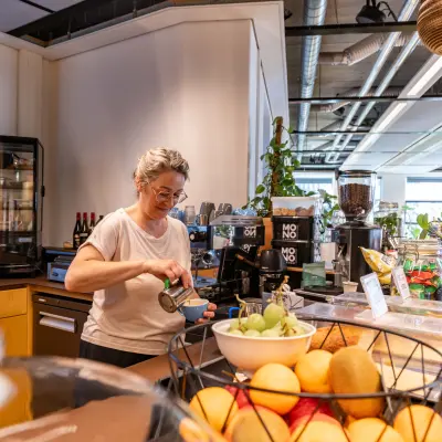 Binnenzicht van kantoorruimte op Fluwelen Burgwal 58, Den Haag Centrum, met een persoon die koffie zet bij een pantry, omringd door fruit en planten.