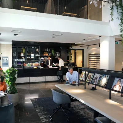Moderne kantoorruimte op Koninginnegracht 19 in Den Haag Centrum, met een stijlvolle ontvangstruimte. Mensen zitten aan tafels en voeren zakelijke gesprekken, met tijdschriften uitgestald voor extra sfeer.