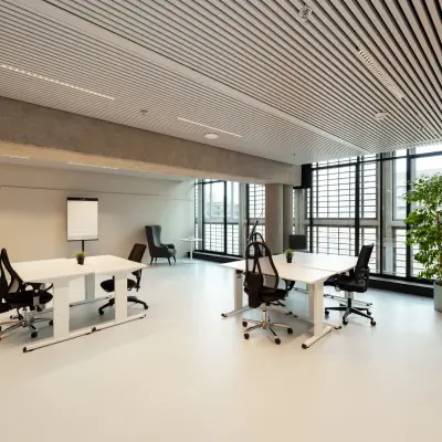 Moderne kantoorruimte te huur op Waldopstraat 5, Den Haag Centrum. Lichte werkruimte met grote ramen, twee bureaus met stoelen en een flipover, ideaal voor creatieve werkprocessen.
