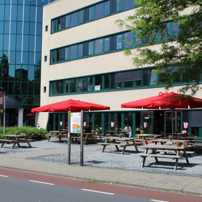 Buitenzicht van een kantoorpand op Keulenstraat 10, Deventer, met tafels onder rode parasols. Ideaal voor kantoorruimte huren met aantrekkelijke buitenfaciliteiten.