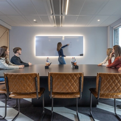 Vergaderruimte in kantoorpand op Flight Forum 120-159, Eindhoven Airport, met zes personen aan tafel en een vrouw die presenteert bij een interactief bord. Kantoorruimte huren voor zakelijke bijeenkomsten.