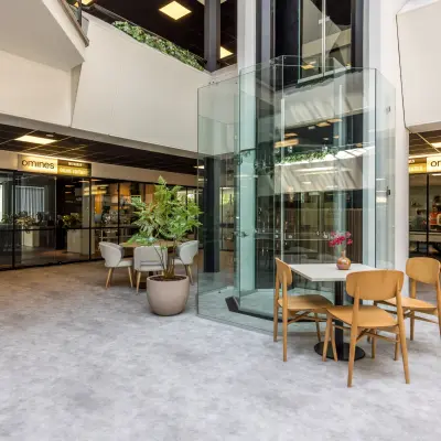 Moderne kantoorruimte huren in Eindhoven Airport met glazen lift en zitgedeelte rondom, ideaal voor flexwerken.