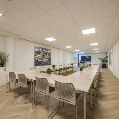Ruime en lichte kantoorruimte met een grote tafel en stoelen, ideaal voor vergaderingen of samenwerking. De ruimte bevindt zich op Luchthavenweg 81, perfect voor kantoorruimte huren op Eindhoven Airport.