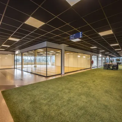 Moderne kantoorruimte te huur op Luchthavenweg 81, Eindhoven Airport, met grote glazen wanden en groene accenten binnen het kantoorpand.