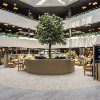 Moderne gemeubileerde kantoorruimte op Luchthavenweg 81, Eindhoven Airport, met een centraal geplaatste boom en mensen die aan tafels werken.
