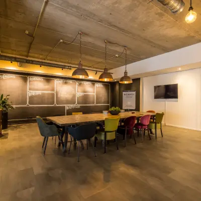 Stijlvolle vergaderzaal met lange houten tafel en gekleurde stoelen, ideaal voor kantoorruimte huren op Eindhoven Airport.