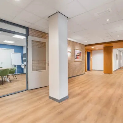 Heldere gang met houten vloer in kantoorpand op Kanaaldijk-Zuid 19, Eindhoven Centrum. Links een vergaderruimte met glazen deuren en modern interieur. Ideale plek voor kantoorruimte huren.