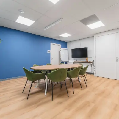 Kantoorruimte met moderne inrichting aan Kanaaldijk-Zuid 19, Eindhoven Centrum, voorzien van een ovale tafel, groene stoelen, een blauw accentmuur en planten, ideaal om te huren.