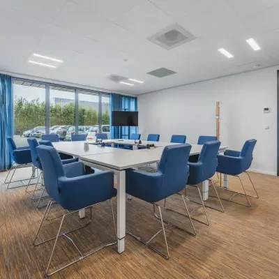 Vergaderruimte met grote tafel en blauwe stoelen, perfect voor kantoorruimte huren op Hurksestraat 60 in Eindhoven De Hurk. Ruime kantoorpandomgeving met moderne faciliteiten voor zakelijke bijeenkomsten.