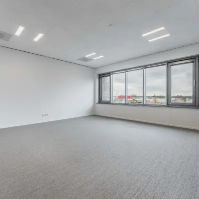Ruime, heldere kantoorruimte te huur in Eindhoven De Hurk met groot raam en grijze vloerbedekking, ideaal voor het inrichten van moderne kantoren.