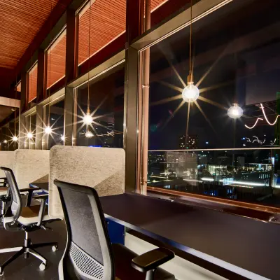 Moderne kantoorruimte met uitzicht op de nachtelijke skyline van Eindhoven, gedeeltelijk gemeubileerd met bureaus en stoelen. Perfect voor wie kantoorruimte wil huren. Gelegen op Achtseweg Zuid 159R, in Strijp-S.