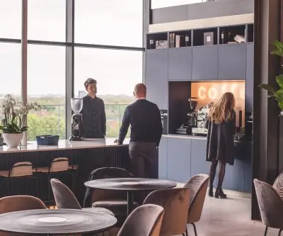 Gezellige kantineruimte in kantoorpand aan Achtseweg Zuid 159R, Eindhoven Strijp-S, met mensen die genieten van een koffiepraatje. Ideaal voor kantoorruimte huren met uitzicht en moderne voorzieningen.