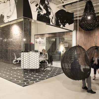 Moderne kantoorruimte huren in Eindhoven Strijp-S op Frederiklaan 10E met glazen wanden, stijlvolle meubels en decoratieve elementen. Personen voeren zakelijke activiteiten uit, zittend in designstoelen.