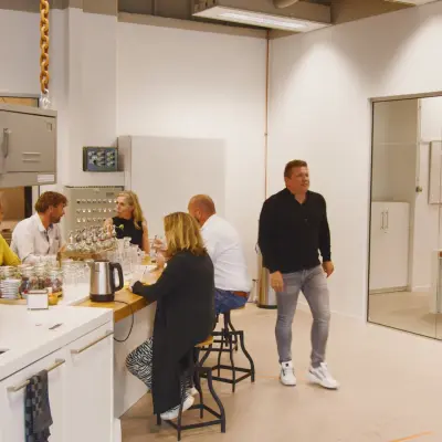 Kantoorruimte in Eindhoven Strijp-S met mensen aan een hoge tafel en een aparte vergaderruimte. Ideaal om kantoor te huren.