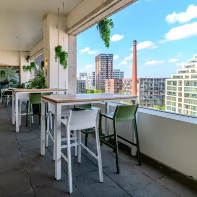 Buitenterras met moderne zitplaatsen en uitzicht op de skyline van Eindhoven Strijp-S, geschikt voor informeel werk of lunchpauzes.