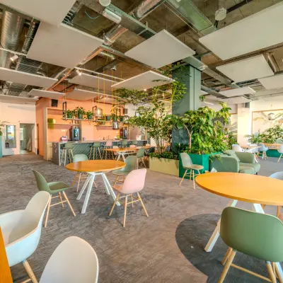 Lichte en groene werkplek in Eindhoven Strijp-S met moderne inrichting en veel planten. Ideale kantoorruimte huren met ronde tafels en comfortabele stoelen.