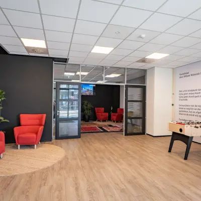 Kantoorruimte huren in Enschede met een moderne entree, voorzien van rode stoelen, tafelvoetbaltafel en decoratieve planten op Kuipersdijk 2-4.