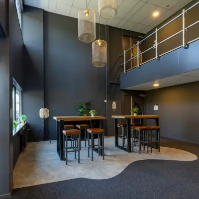 Kantoorruimte in Enschede bij Marssteden 20 met hoge plafonds, een moderne zithoek met tafels en krukken, en voldoende lichtinval. Ideaal voor bedrijven die een kantoorpand willen huren.