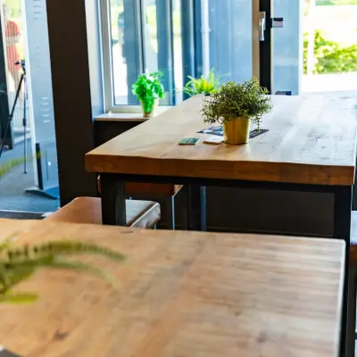 Moderne kantoorruimte in Enschede met houten tafels en hoge krukken bij grote ramen, voor een inspirerende werkplek in het kantoorpand op Marssteden 20. Ideaal voor kantoorruimte huren.