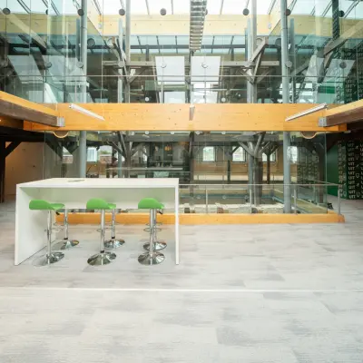 Moderne kantoorruimte huren op Prins Hendrikkade 3 in Franeker, met hoge plafonds, glazen elementen en comfortabele zitplaatsen aan een witte hoge tafel in het kantoorpand.