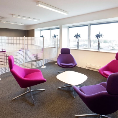 Kantoorruimte huren in Geleen met moderne paarse stoelen en bijzettafels, natuurlijk licht door grote ramen, ideaal voor een ontspannen werkomgeving.