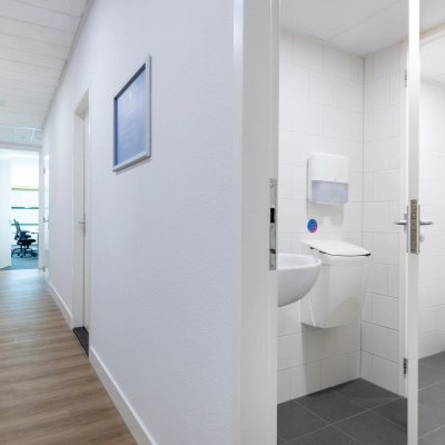 Kantoorcorridor met houten vloer, witte muren en een toilet aan de rechterkant op Groningenweg 8 8, Gouda. Perfect om een kantoorruimte te huren.
