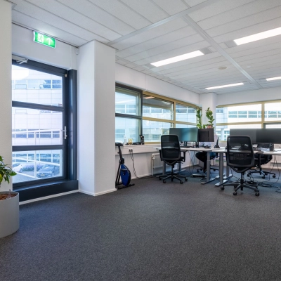Heldere kantoorruimte met vier bureaus, stoelen en een plant in een kantoorpand op Groningenweg 8 8 in Gouda. Grote ramen zorgen voor veel licht. Ideaal voor wie kantoorruimte wil huren.
