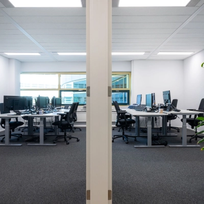 Moderne kantoorruimte in Gouda met meerdere bureaus en computers, geschikt voor zakelijke activiteiten. Grote ramen zorgen voor natuurlijk licht in het kantoorpand.