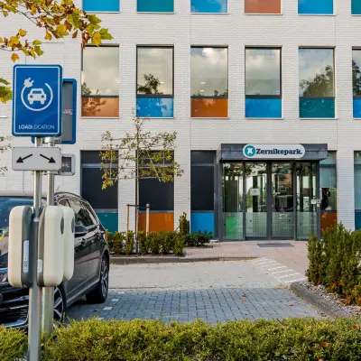 Vooraanzicht van het kantoorpand aan Zernikepark 12 in Groningen met kleurrijke raampartijen en laadpunt voor elektrische auto's.