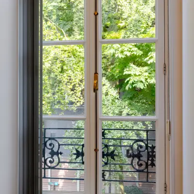 Uitzicht door een groot raam met smeedijzeren balkon, groene bomen buiten. Ideaal voor kantoorruimte huren in Haarlem Centraal Station, Kennemerplein 20.