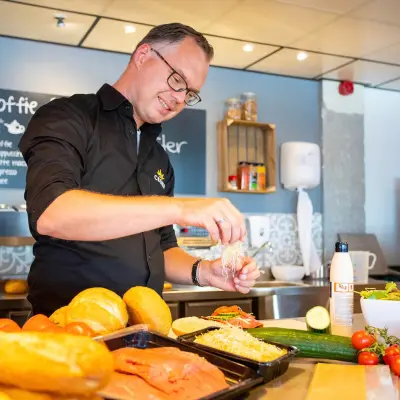 Kantoorruimte huren in kantoorpand op A. Hofmanweg 5A, Haarlem Waarderpolder. Persoon bereidt eten in gemeubileerde keukenruimte met broodjes, groenten en koffieapparaat op de achtergrond.