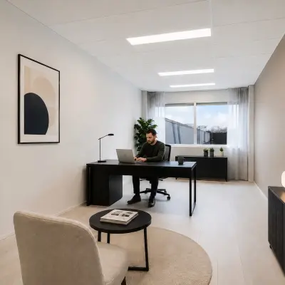 Stijlvolle en moderne kantoorruimte met een persoon die aan het werk is op een laptop aan een strak bureau, omgeven door planten en kunst aan de muur.