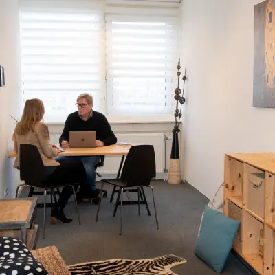 Gezellige kantoorkamer op Waarderweg 19 in Haarlem Waarderpolder met houten meubels en kunst aan de muur. Twee personen voeren een zakelijk gesprek aan een bureau. Mogelijkheid voor kantoorruimte huren.