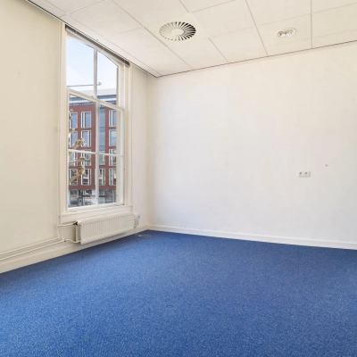 Leeg kantoorpand op Houtplein 22, Haarlem Zuid met blauwe vloerbedekking en grote ramen die daglicht binnenlaten, ideaal voor een creatieve inrichting voor wie kantoorruimte wil huren.