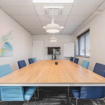 Heldere vergaderruimte met een lange tafel en kleurrijke stoelen, ideaal voor kantoorruimte huren in Helmond.