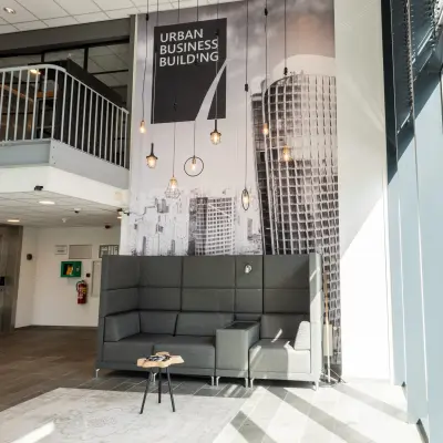 In het kantoorpand op Demmersweg 3, Hengelo, een moderne loungehoek met hoge grijze bank en industriële verlichting. Zoek je kantoorruimte te huur? Hier vind je inspiratie en comfort.