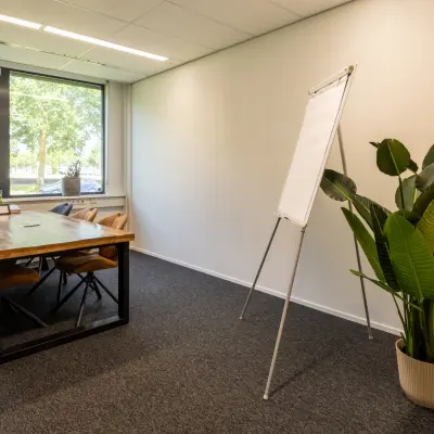 Kantoorruimte huren op Jan Tinbergenstraat 202, Hengelo: een helder kantoor met grote ramen, houten tafel, stoelen en planten. Ideaal voor creatieve en productieve momenten.