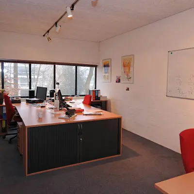 Kantoorruimte te huur aan de Catharina van Renneslaan 8-10 in Hilversum met grote ramen, diverse bureaus en rode stoelen, witte muren en een whiteboard.