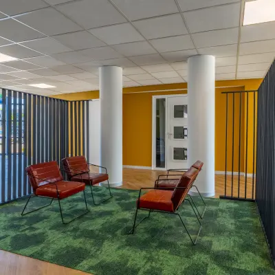 Moderne kantoorruimte met kleurrijke muren en comfortabele zithoek, ideaal voor informele vergaderingen of pauzes. Glaswand zorgt voor veel licht en een uitnodigende sfeer om te werken.
