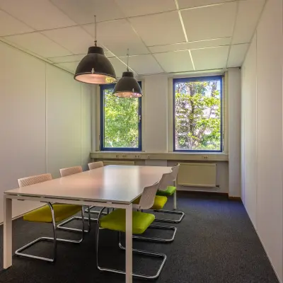 Kantoorruimte te huur aan de Franciscusweg 219 in Hilversum. Het interieur heeft een vergadertafel met stoelen, grote ramen geven zicht op groen buiten.