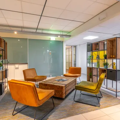 Moderne kantoorruimte met kleurrijke fauteuils en houten tafels op Mozartlaan 27, Hilversum. De ruimte is ingericht met trendy meubels en planten, ideaal voor een warme en uitnodigende werkomgeving.