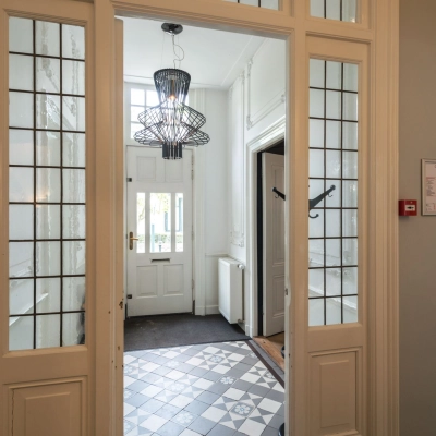 Ingang van een kantoorpand aan de Oude Enghweg 8 in Hilversum met glazen deuren en een decoratieve tegelvloer. Ideale plek om kantoorruimte te huren.