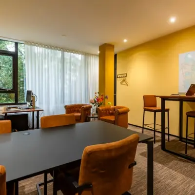 Kantoorruimte huren op Steijnlaan 16 in Hilversum met gele muren, grote ramen, enkele bureaus, tafels en stoelen, en een kaart aan de muur.