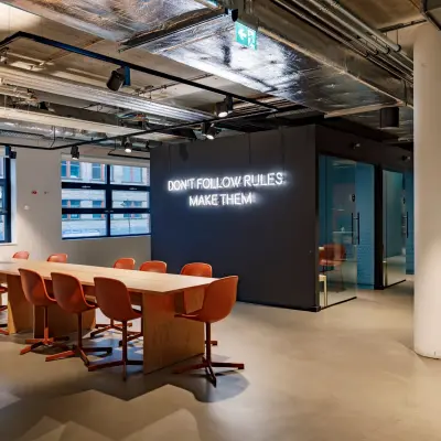 Moderne kantoorruimte op Siriusdreef 16 in Hoofddorp met een lange tafel en oranje stoelen, geschikt voor vergaderingen of teamwerk. De muur heeft inspirerende tekst, ideaal voor wie kantoorruimte wil huren.