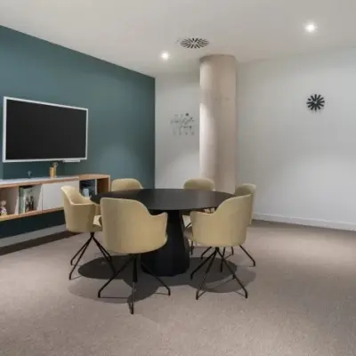 Moderne vergaderruimte met zes beige stoelen rondom een ovale tafel, een muur met een klok en een scherm, ideaal voor kantoorruimte huren op Siriusdreef 17 in Hoofddorp.